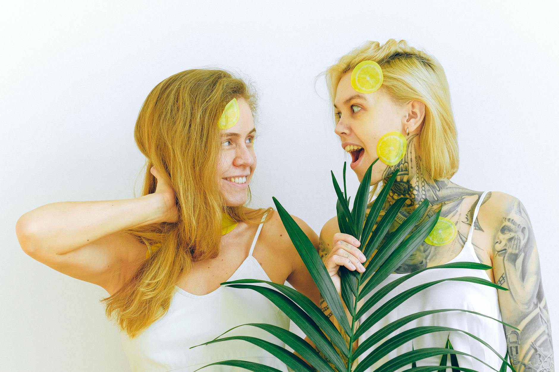 Due donne che sorridono con fette di limone e pianta tropicale, esprimendo gioia e divertimento al chiuso.