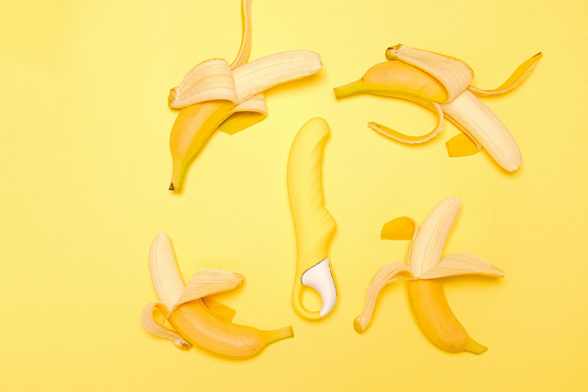 Yellow lemon-shaped vibrator surrounded by fresh lemons on a bright yellow background.