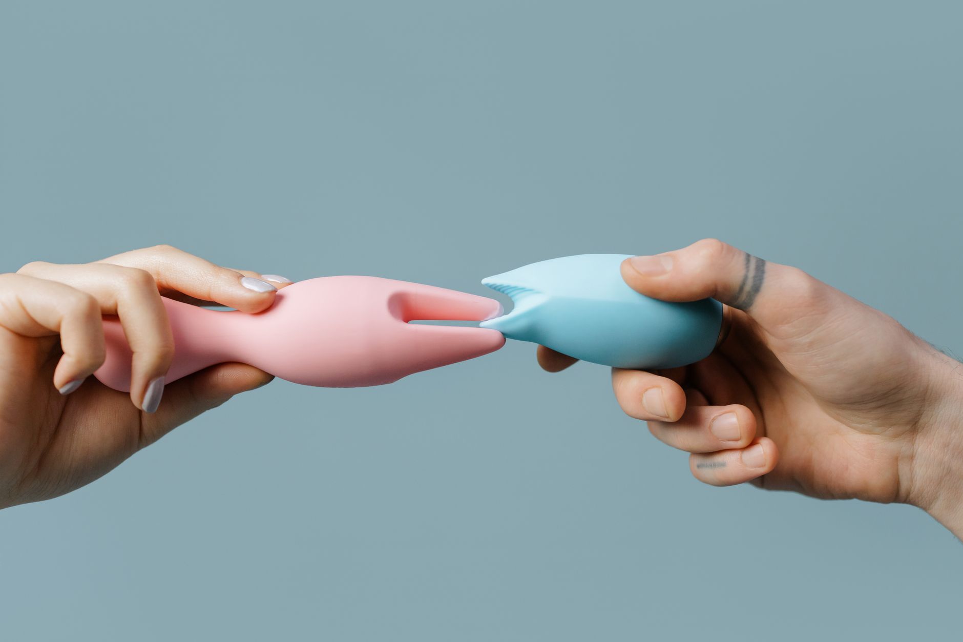Donna con occhiali che tiene in mano due vibratori colorati su sfondo viola