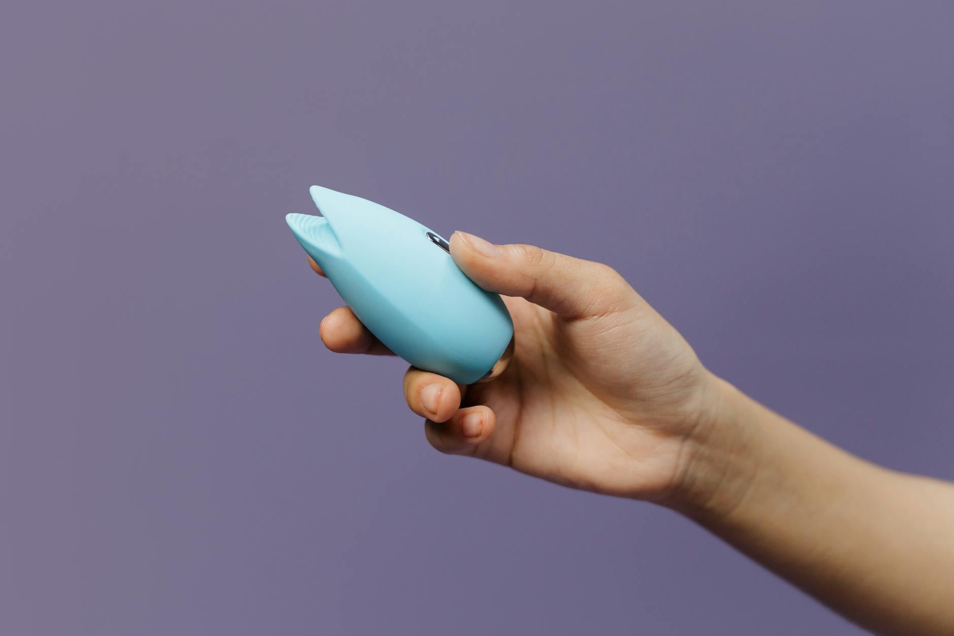 Due mani tengono vibratori rosa e blu su uno sfondo pastello, simboleggiando l'intimità condivisa nelle coppie.