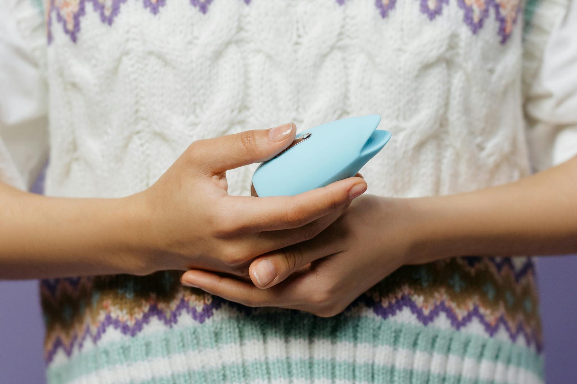 Close-up of hands holding a blue personal massager against a knitted sweater